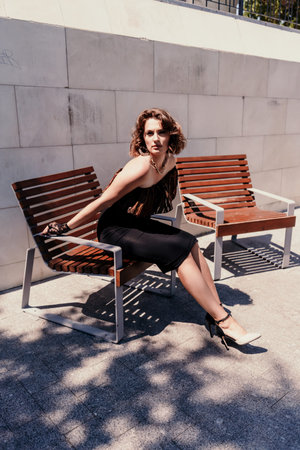 Portrait of a woman on the street. An attractive woman in a black dress is sitting on a bench...