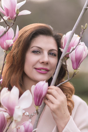 Woman magnolia flowers, surrounded by blossoming trees., hair down, wearing a light coat. Captured during spring, showcasing natural beauty and seasonal change.の写真素材