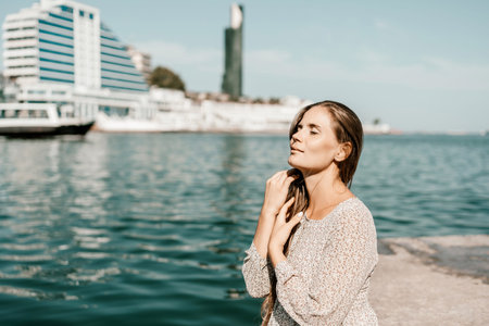 A woman is sitting in the water wearing a white dress. The water is calm and blue. The woman is...