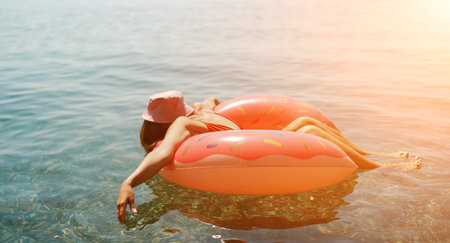 Summer vacation woman in hat floats on an inflatable donut mattress. Happy woman relaxing and...