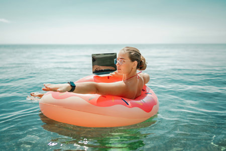 Woman laptop sea. Freelancer woman in sunglases floating on an inflatable big pink donut with a...