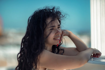 Sea woman rest. Portrait of a woman with long curly black hair in a beige dress stands on a balcony...