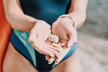 Beach vacation snapshot: A woman in a swimsuit holding a pebble in her hands, enjoying the serenity of the beach and the beauty of nature, creating a peaceful and relaxing atmosphere.の写真素材
