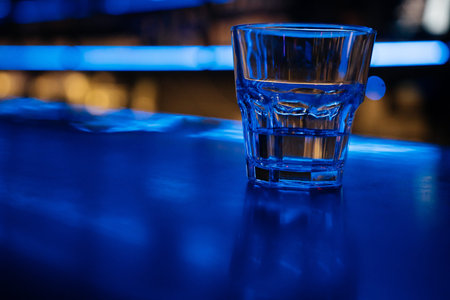 A glass of water sits on a bar counter. The bar is dimly lit, giving the scene a cozy and intimate...