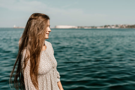 A woman is walking on the beach wearing a dress. The water is calm and the sky is clear.の写真素材