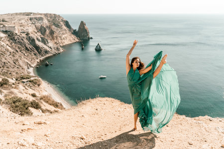 Woman green dress sea. Female dancer posing on a rocky outcrop high above the sea. Girl on the nature on blue sky background. Fashion photo.の写真素材