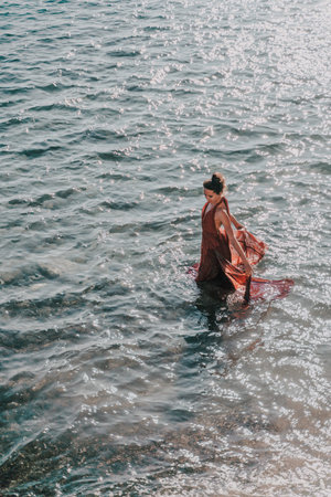Woman red dress sea. Female dancer in a long red dress posing on a beach with rocks on sunny day
