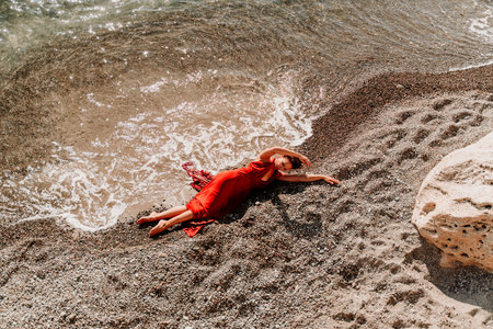 Woman red dress sea. Female dancer in a long red dress posing on a beach with rocks on sunny day