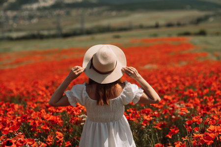 Field poppies woman. Happy woman in a white dress and hat stand through a blooming field of poppy raised her hands up. Field of blooming poppies.の写真素材
