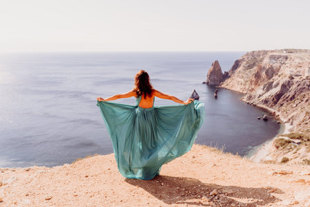 Woman green dress sea. Female dancer posing on a rocky outcrop high above the sea. Girl on the nature on blue sky background. Fashion photo.の写真素材