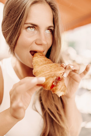 A woman is eating a croissant. The croissant is half eaten and has a jelly filling.の写真素材