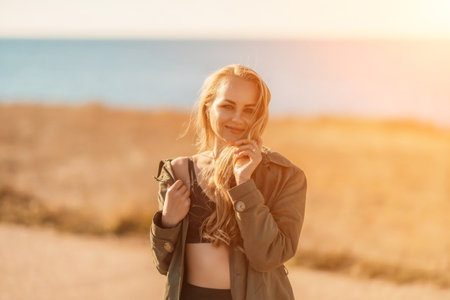 Portrait blonde sea cape. A calm young blonde in an unbuttoned khaki raincoat stands on the seashore, under the raincoat there is a black skirt and topの写真素材