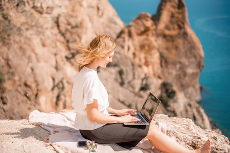 Freelance woman working on a laptop by the sea, typing away on the keyboard while enjoying the...