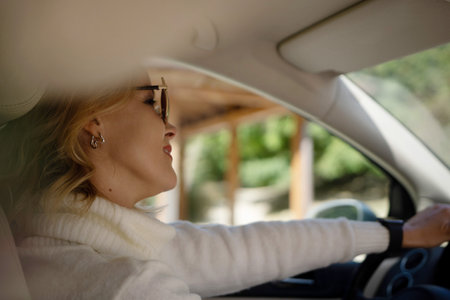 A blonde woman in a white sweater and jeans is driving. Happy woman sitting in a car with a white interior.の写真素材