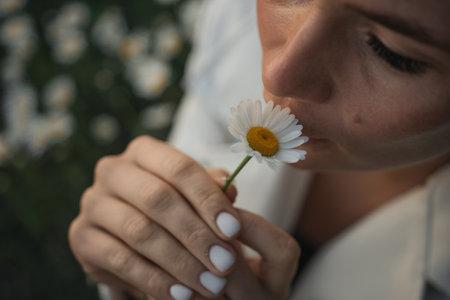 A woman is smelling a flower. The flower is white and yellow.の写真素材