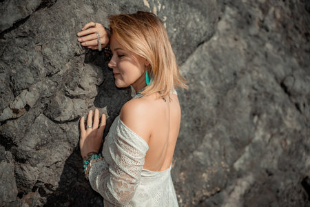 Middle aged woman looks good with blond hair, boho style in white long dress on the beach decorations on her neck and arms.の写真素材