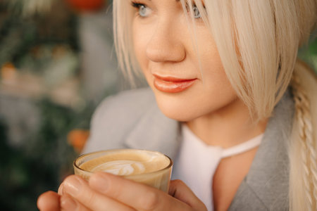A blonde woman is holding a cup of coffee. She is wearing a gray jacket and white shirt.の写真素材