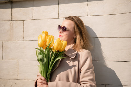 Woman holding yellow tulips, leaning against stone wall. Womens holiday concept, giving flowers.の写真素材