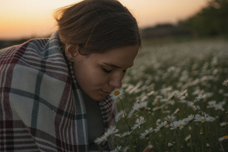 A woman is sniffing a flower in a field. The scene is peaceful and serene, with the woman enjoying the beauty of nature.の写真素材