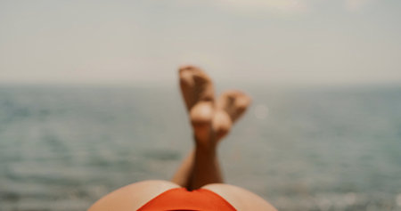 A woman sunbathes on the beach, lying on her stomach in a red swimsuit against the sea backdrop.の写真素材