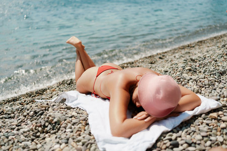 A woman sunbathes on the beach, lying on her stomach in a red swimsuit against the sea backdrop.の写真素材
