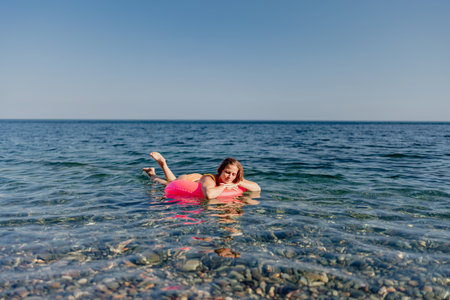 A woman is floating on a pink inflatable raft in the oceanの写真素材