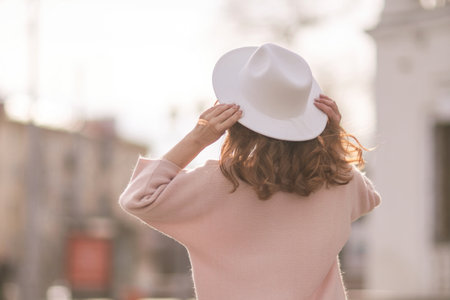 A woman wearing a white hat and a pink sweater stands in front of a buildingの写真素材
