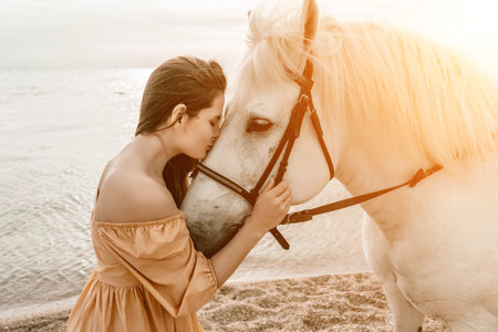 A woman in a dress stands next to a white horse on a beach, with the blue sky and sea in the background.の写真素材