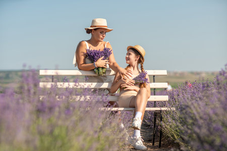 woman child sitting bench in field lavender. The woman is holding a bouquet of flowers, and the child is holding a bouquet as well. The scene is peaceful and serene.の写真素材