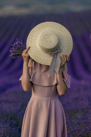 A woman wearing a hat and holding a bunch of lavender flowersの写真素材