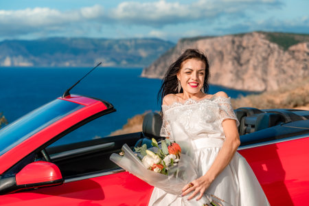 A woman in a white dress stands in front of a red convertible car. She is holding a bouquet of flowers and smiling. Concept of happiness and celebration.の写真素材