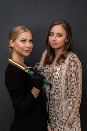 Two women are posing for a photo, one holding a hair curler. Scene is casual and friendly, as the women are smiling and looking at the camera.の写真素材