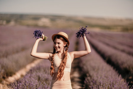 girl is holding a bunch of lavender purple flowers in her hands and wearing a straw hat. She is smiling and she is enjoying herself. The scene is set in a field of lavender, which adds to the peaceful.の写真素材