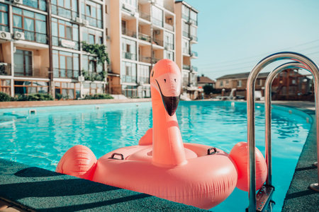 A pink flamingo float is floating in a pool. The flamingo is in the middle of the pool and is surrounded by water. The pool is located in a building with a lot of windows.の写真素材