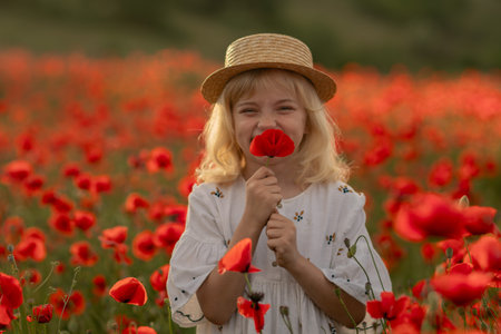 A young girl is standing in a field of red poppies, holding a flower in her handの写真素材