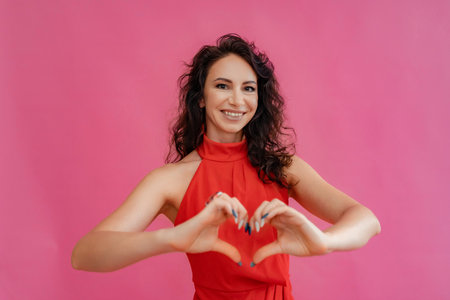 A woman in a red dress is smiling and holding her hands together to make a heart shape. Concept of love and happiness.の写真素材