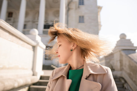 A woman with long hair is standing on a set of stairs. She is wearing a green shirt and a tan coat.の写真素材