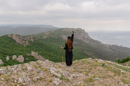 A woman stands on a mountain top, holding a walking stickの写真素材