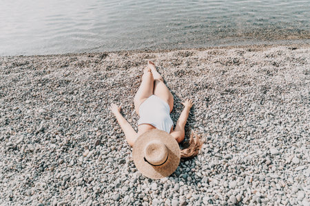 A woman is laying on the beach wearing a straw hat. She is wearing a white bikini top and white bikini bottoms.の写真素材