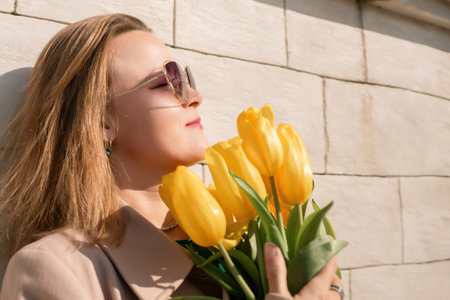 Woman holding yellow tulips, leaning against stone wall. Womens holiday concept, giving flowers.の写真素材