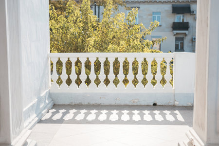 A balcony with a railing and a tree in the background. The railing is white and has a shadow on it.の写真素材