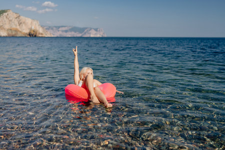A young girl is floating on a red inflatable raft in the oceanの写真素材
