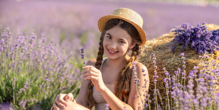 A young girl is sitting in a field of purple flowers, holding a purple flower in her hand. She is smiling and she is enjoying the moment. Concept of happiness and contentment.の写真素材