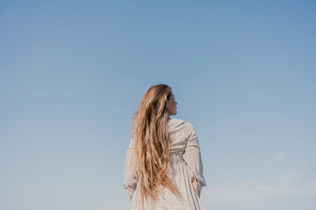 woman with long hair stands in front of a blue sky. She is wearing a white and black striped shirt.