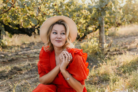 A woman in a red dress is sitting in a field with a straw hat onの写真素材