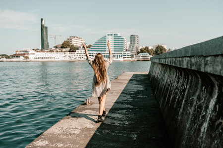 woman in a white dress is walking on a pier near the water. The scene is peaceful and serene, with the womans long hair blowing in the wind.の写真素材