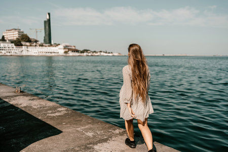 woman in a white dress is walking on a pier near the water. The scene is peaceful and serene, with the womans long hair blowing in the wind.の写真素材