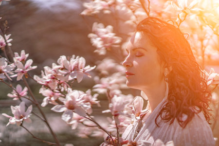 Magnolia park woman. Stylish woman in a hat stands near the magnolia bush in the park. Dressed in white corset pants and posing for the camera.の写真素材