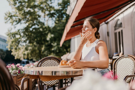 Portrait of happy woman sitting in a cafe outdoor drinking coffee. Woman while relaxing in cafe at table on street, dressed in a white T-shirt and jeansの写真素材