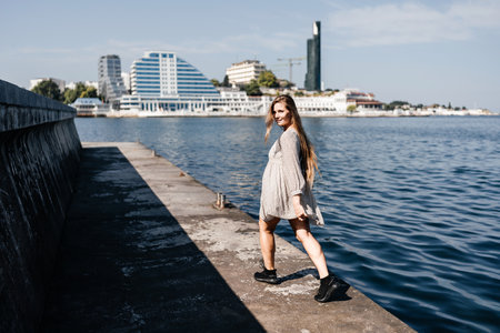 woman in a white dress is walking on a pier near the water. The scene is peaceful and serene, with the womans long hair blowing in the wind.の写真素材
